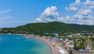 Dağın eteğinde turistlerle dolu bir plajı olan bir tatil beldesi.