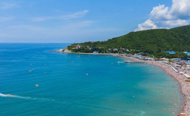 Dağın eteğinde turistlerle dolu bir plajı olan bir tatil beldesi.