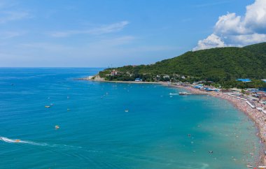 Dağın eteğinde turistlerle dolu bir plajı olan bir tatil beldesi.