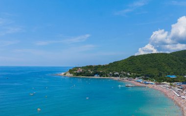 Dağın eteğinde turistlerle dolu bir plajı olan bir tatil beldesi.