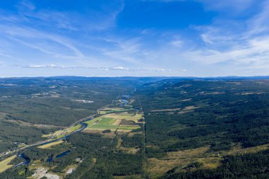 Geniş bir nehir vadisinin uçsuz bucaksız mavi gökyüzünün altında uzanan nefes kesici panoramik hava manzarası. Vadiden akan kıvrımlı bir nehir her iki taraftaki yemyeşil ormanlarla çevrili..