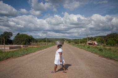 Barra de Aroeira, Santa Tereza do Tocantins, Tocantins, Brezilya - 7 Mayıs 2016: Kafasında devasa demir tepsi taşıyan Quilombola kadını, quilombo Barra de Aroeira 'dan geçen asfalt yoldan geçiyor