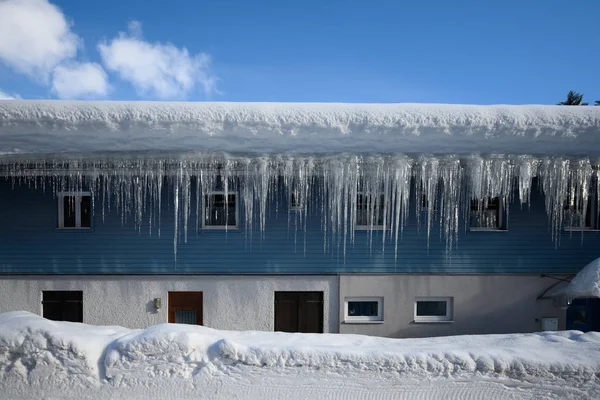 Ijspegel op dak van huis in de winter met blauwe lucht — Stockfoto