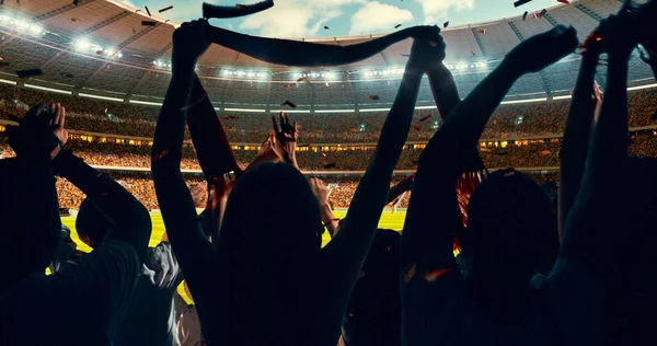 Group of cheering fans watch a sport championship on stadium. Their team wins and everybody are celebrating this event. People are dressed in casual cloth.