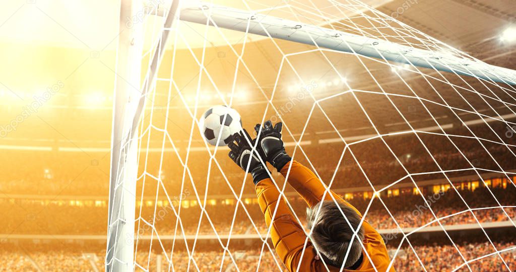 Goalkeeper tries to save from a goal on a professional soccer stadium while the sun shines. Stadium and crowd are made in 3D.