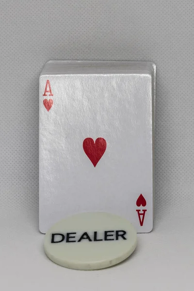 A deck of poker cards with a plaque bearing the inscription dealer. There is an ace of hearts on the card.