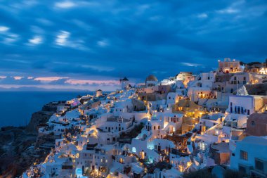 Günbatımından sonra Yunanistan 'ın Santorini kentindeki Oia kasabasının akşam manzarası. Güzel bulutlar uzun zaman aldı. Arka plan mavi saatte gökyüzü. Beyaz evlerde ışıklar parlıyor..