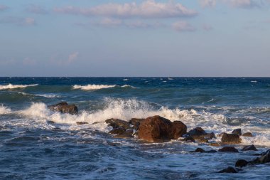 Vlichada 'da kıyıları ve denizi olan güzel, siyah bir sahil. Mavi gökyüzü arka planında beyaz bulutlar ve deniz var..