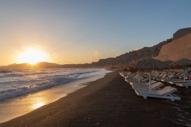 Yunanistan 'ın Santorini adasındaki Vlychada plajında güzel bir sahil. Denizin arka planında yükselen güneşli mavi bir gökyüzü var..