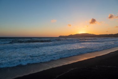 Yunanistan 'ın Santorini adasındaki Vlychada plajında güzel bir sahil. Denizin arka planında yükselen güneşli mavi bir gökyüzü var..