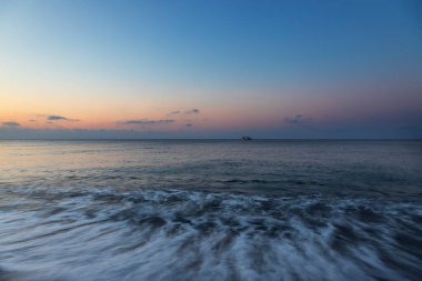 Yunanistan 'ın Santorini adasında güneş doğarken Perivolos plajı. Arka plan beyaz bulutlu mavi bir gökyüzü..