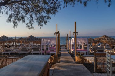 Yunanistan 'ın Santorini adasında güneş doğarken Perivolos plajı. Arka plan beyaz bulutlu mavi bir gökyüzü..