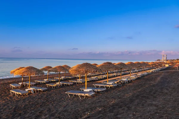 Yunanistan 'ın Santorini adasında güneş doğarken Perivolos plajı. Arka plan beyaz bulutlu mavi bir gökyüzü..