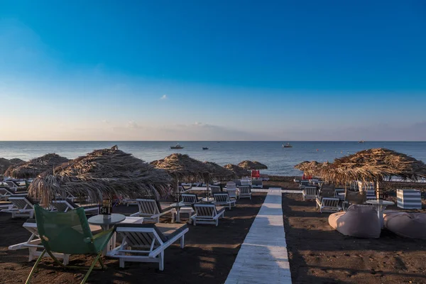 Yunanistan 'ın Santorini adasında güneş doğarken Perivolos plajı. Arka plan beyaz bulutlu mavi bir gökyüzü..