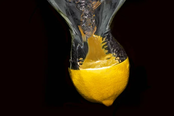 Half a lemon thrown into the water. Bubbles of water come from the lemon. The photo has a black background.
