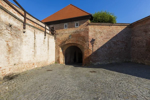 Birbirine kenetlenmiş asfaltı olan bir avlu. Kenarlarında tuğla duvarlar var..