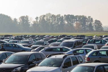 Yeşil alana park edilmiş arabalar. Arka planda bir orman var..