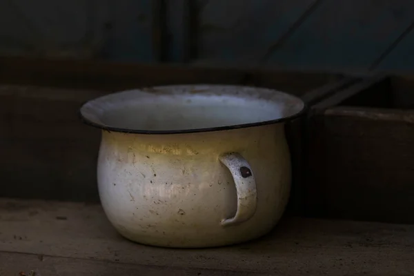 Ahşap bir rafta duran teneke, eski, beyaz bir lazımlık. Arka plan karanlık..