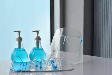 Şeffaf plastik yüz bakımı, yeşil dezenfektanlar ve cam kapının önündeki yeşil tıbbi maske. Yüze ve ellere sürtünmek için. Antikoronavirüs ya da covid-19 konsepti..