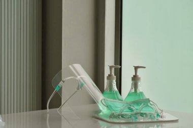 Şeffaf plastik yüz bakımı, yeşil dezenfektanlar ve cam kapının önündeki yeşil tıbbi maske. Yüze ve ellere sürtünmek için. Antikoronavirüs ya da covid-19 konsepti..