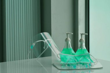 Şeffaf plastik yüz bakımı, yeşil dezenfektanlar ve cam kapının önündeki yeşil tıbbi maske. Yüze ve ellere sürtünmek için. Antikoronavirüs ya da covid-19 konsepti..