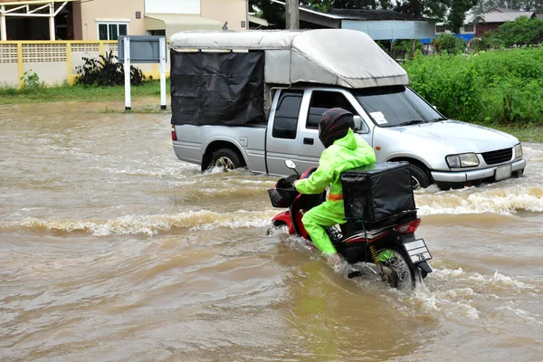 Food delivery rider is riding his motorbike passing the floodwater