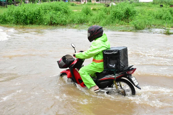 Food delivery rider is riding his motorbike passing the floodwater