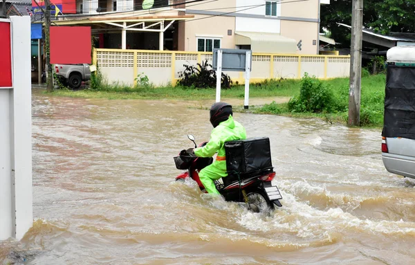 Food delivery rider is riding his motorbike passing the floodwater