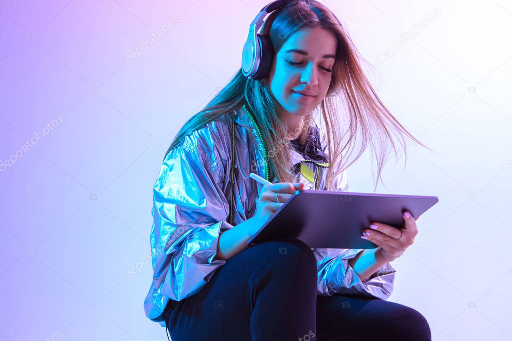 Modern Girl with laptop, tablet computer. Free creativity. Young blogger makes a Home office. Colored Neon light and background.