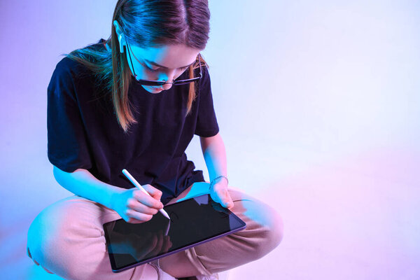 Modern Girl with laptop, tablet computer. Free creativity. A young blogger makes a Home office. Colored Neon light and background.