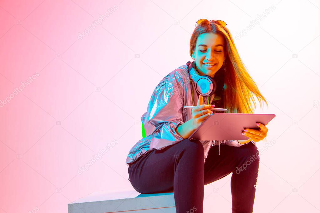 Modern Girl with laptop, tablet computer. Free creativity. A young blogger makes a Home office. Colored Neon light and background.