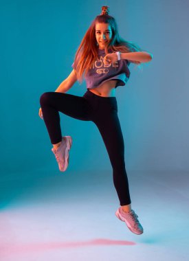 Stüdyoda renkli neon arka planda zumba yapan genç ve şık bir kız. Dans posteri tasarımı.