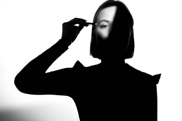 Portrait of a girl on a white background. Fashion model uses cosmetic pencil for eyebrows and eyelids. Black-white.