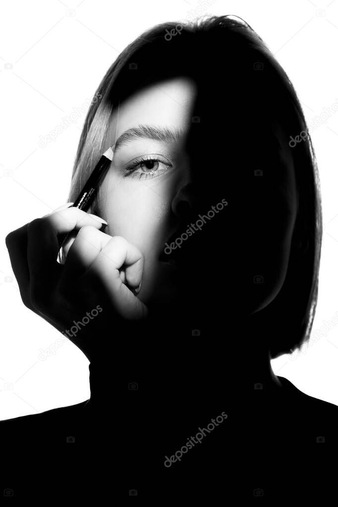 Portrait of a girl on a white background. Fashion model uses cosmetic pencil for eyebrows and eyelids. Black-white.