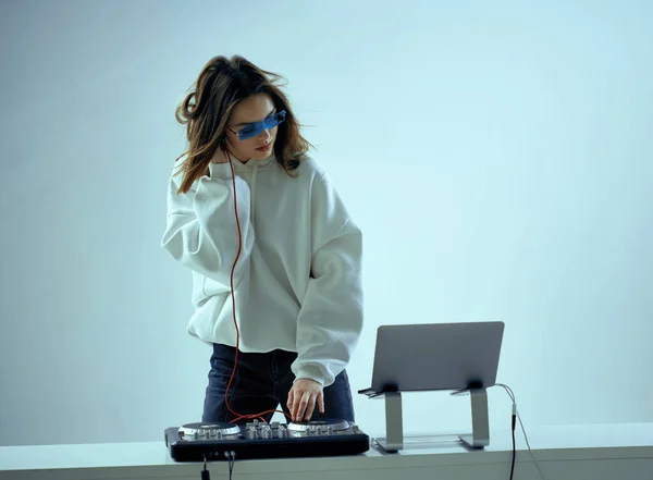 Cool fiatal lány DJ keveri a zenét egy keverő konzol és laptop, elegáns ruhák, szemüveg egy neon háttér. — Stock Fotó