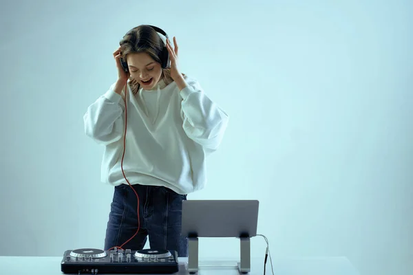 Cool mladá dívka DJ míchá hudbu na mixážní konzoli a notebook, ve stylovém oblečení, na bílém modrém pozadí. — Stock fotografie