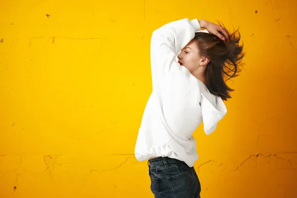 Porträt einer jungen hübschen Studentin in weißem Kapuzenpulli, legerer Kleidung vor einer orangefarbenen Betonwand. — Stockfoto