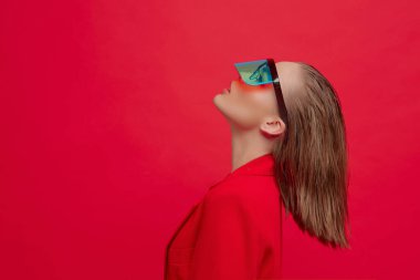 Havalı bir stil kızı, şık bir saç stili ve parlak kırmızı arka planda büyük cam pozlar veren şık gözlükleri var.