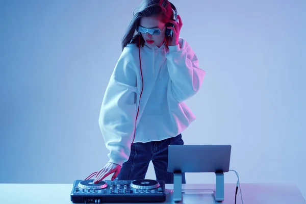 Cool fiatal lány DJ keveri a zenét egy keverő konzol és laptop, elegáns ruhák, szemüveg egy neon háttér. — Stock Fotó