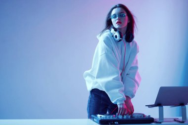 Havalı genç kız DJ karışık konsol ve dizüstü bilgisayarda müziği karıştırıyor, şık kıyafetler içinde, neon arka planda gözlük takıyor..