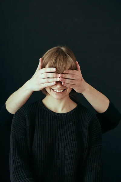 Мужские руки закрывают глаза довольно счастливой девушки с улыбкой на черном фоне крупным планом . — стоковое фото