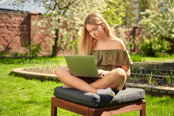 Kreatív fiatal lány blogger dolgozik egy laptop tartalmat ül a hátsó udvaron egy ház a kertben a gyep. — Stock Fotó