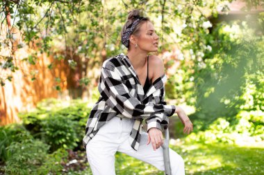 Elinde kürekle şık bir genç kız güneşli bir yaz gününde arka bahçede poz veriyor..