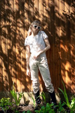 Güneşli bir günde, arka bahçede ahşap bir çite karşı duran gözlüklü ve başörtülü güzel bir kızın portresi..