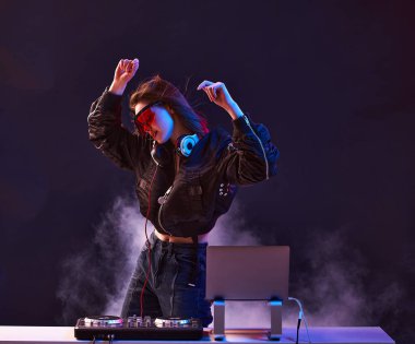 Gözlüklü şık bir DJ ve bir bombacı, dumandaki neon ışıkta dans eden bir partide müziği karıştırıyor. .