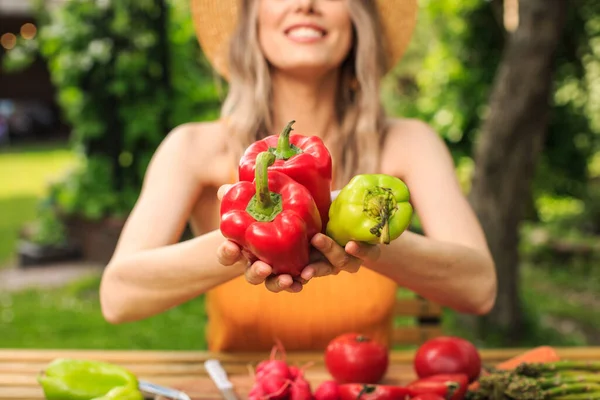 Gadis cantik dengan topi duduk di meja kayu dengan sayuran segar tumbuh di kebunnya di musim panas. tutup — Stok Foto