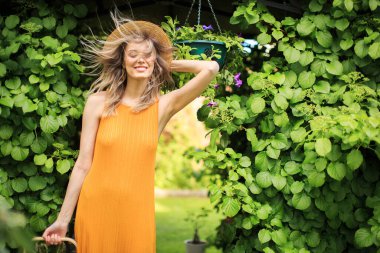 Şapkalı, sepetli, rüzgârlı yeşil bahçeli genç kız blog ve reklamcılık için fotoğraf.