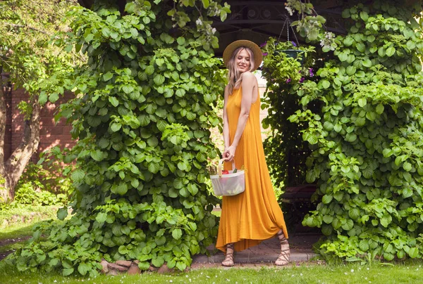 Joven chica sonriente en sombrero en el jardín verde de verano con cesta de verduras frescas, fotografía para blog y publicidad —  Fotos de Stock