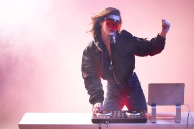 Gözlüklü şık bir DJ ve bir bombacı, dumandaki neon ışıkta dans eden bir partide müziği karıştırıyor. .