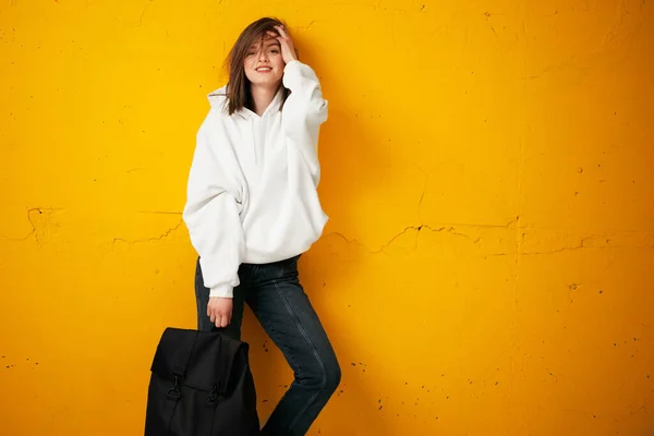 Retrato de una joven estudiante guapa con capucha blanca, ropa casual, con una bolsa, contra una pared de hormigón naranja . —  Fotos de Stock